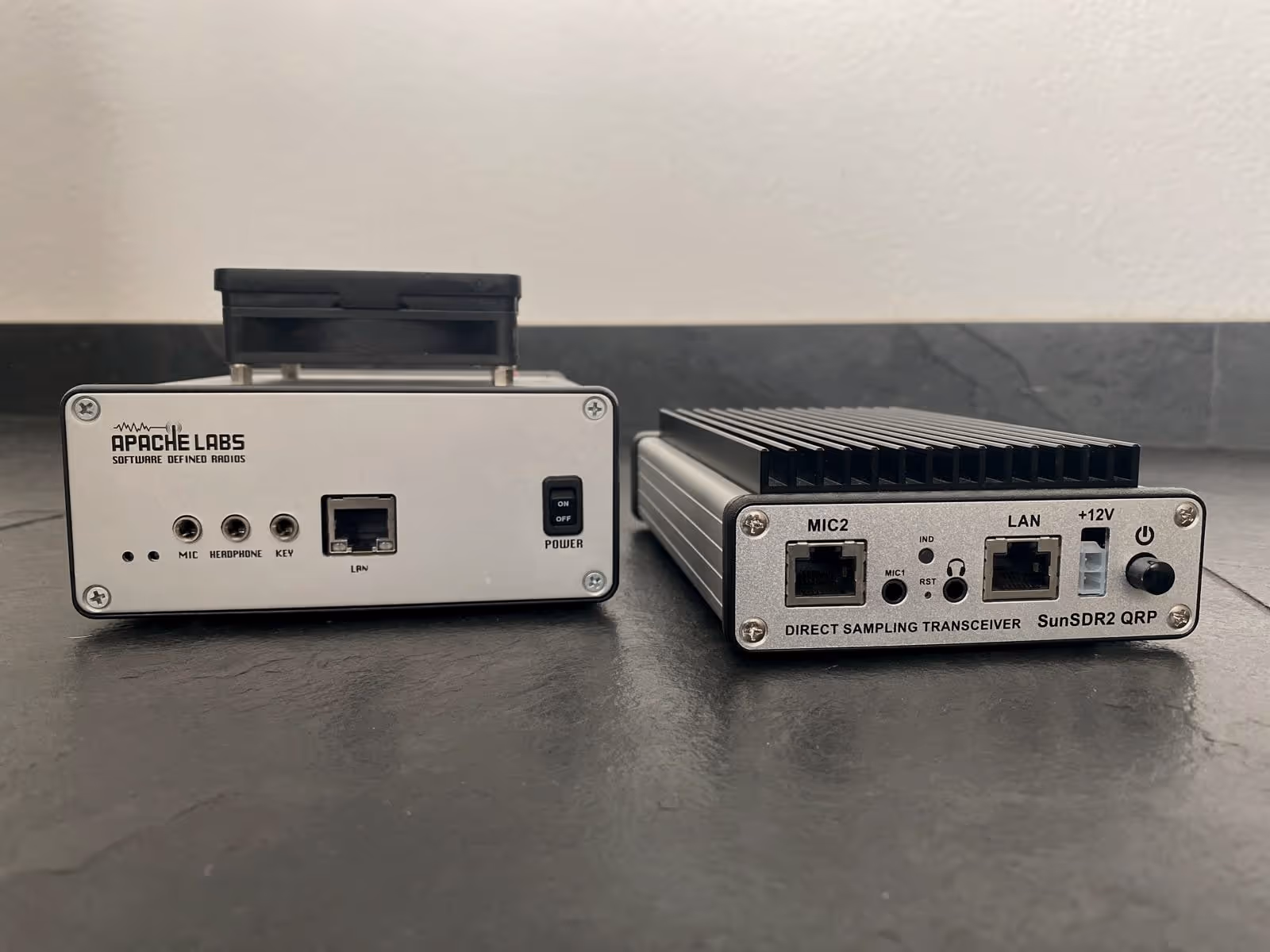 Dos equipos de radio uno junto al otro: a la izquierda un ANAN-10E de Apache Labs con un ventilador encima, a la derecha un SunSDR2 QRP con un gran disipador