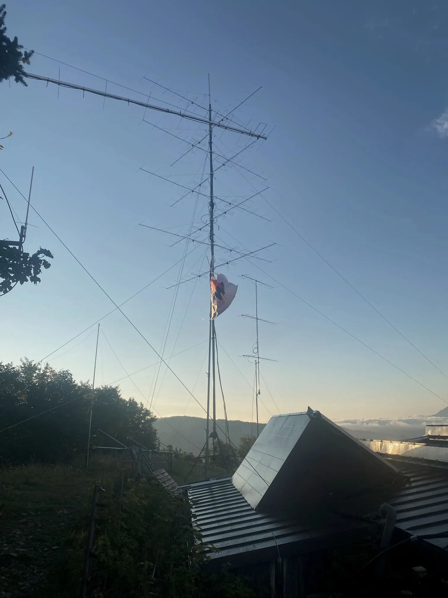 El mástil grande con los grupos apilados bajo luz rasante, la bandera y los tejados de la cabaña al lado