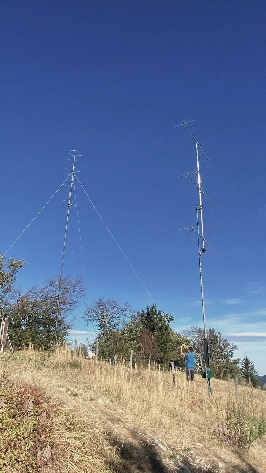 Dos mástiles en el prado contra un cielo azul intenso, alguien trabajando en el mástil de la derecha