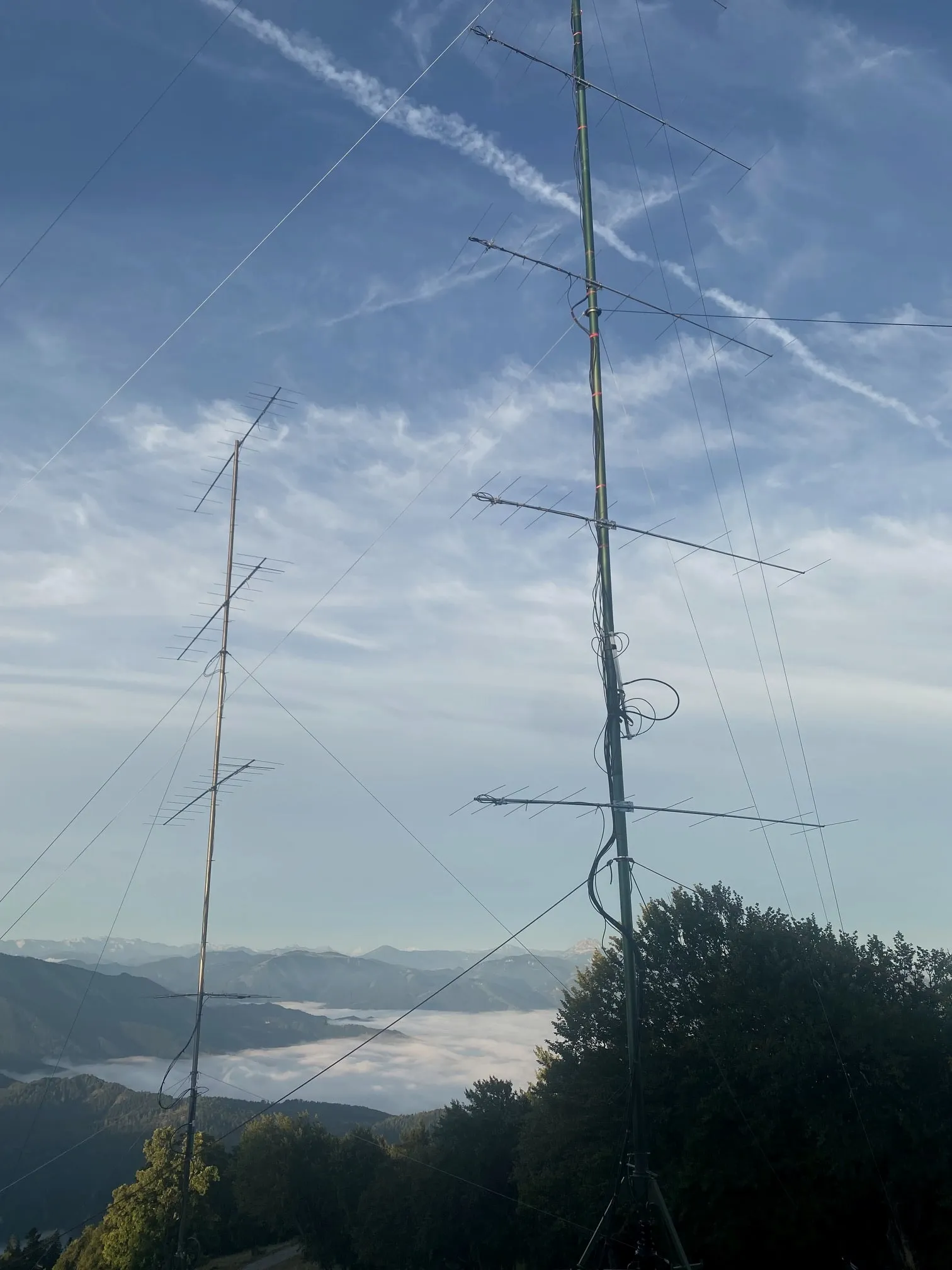 Dos mástiles de antena sobre un mar de niebla cerrado, los Alpes detrás