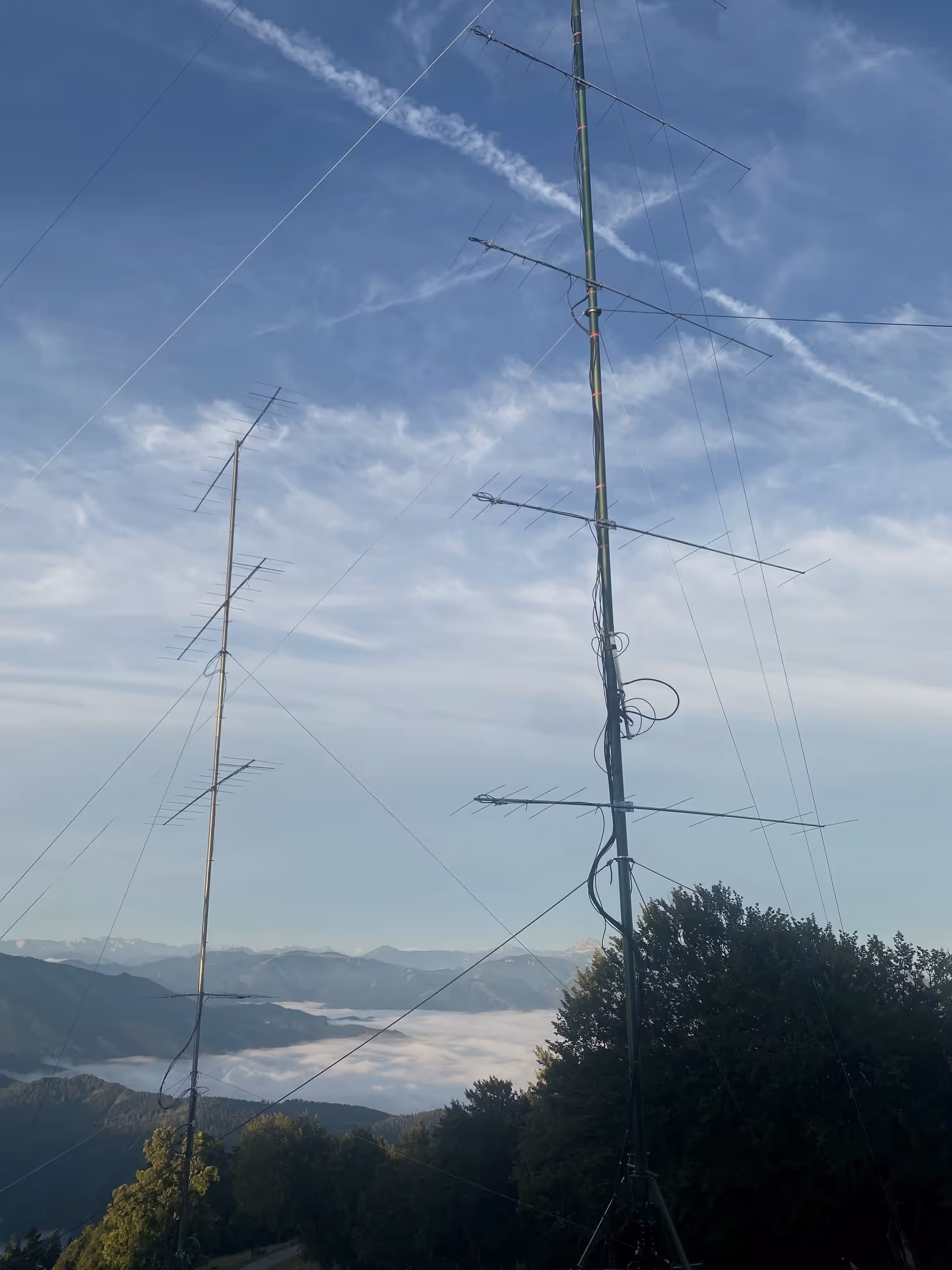 Dos mástiles de antena sobre un mar de niebla cerrado, los Alpes detrás