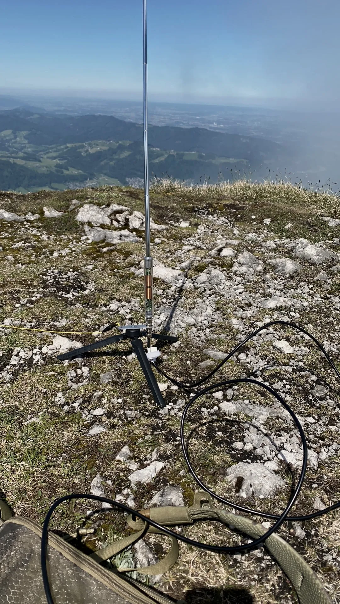 El radiador telescópico con bobina sobre un trípode en la cumbre rocosa, detrás la vista hacia el antepaís alpino