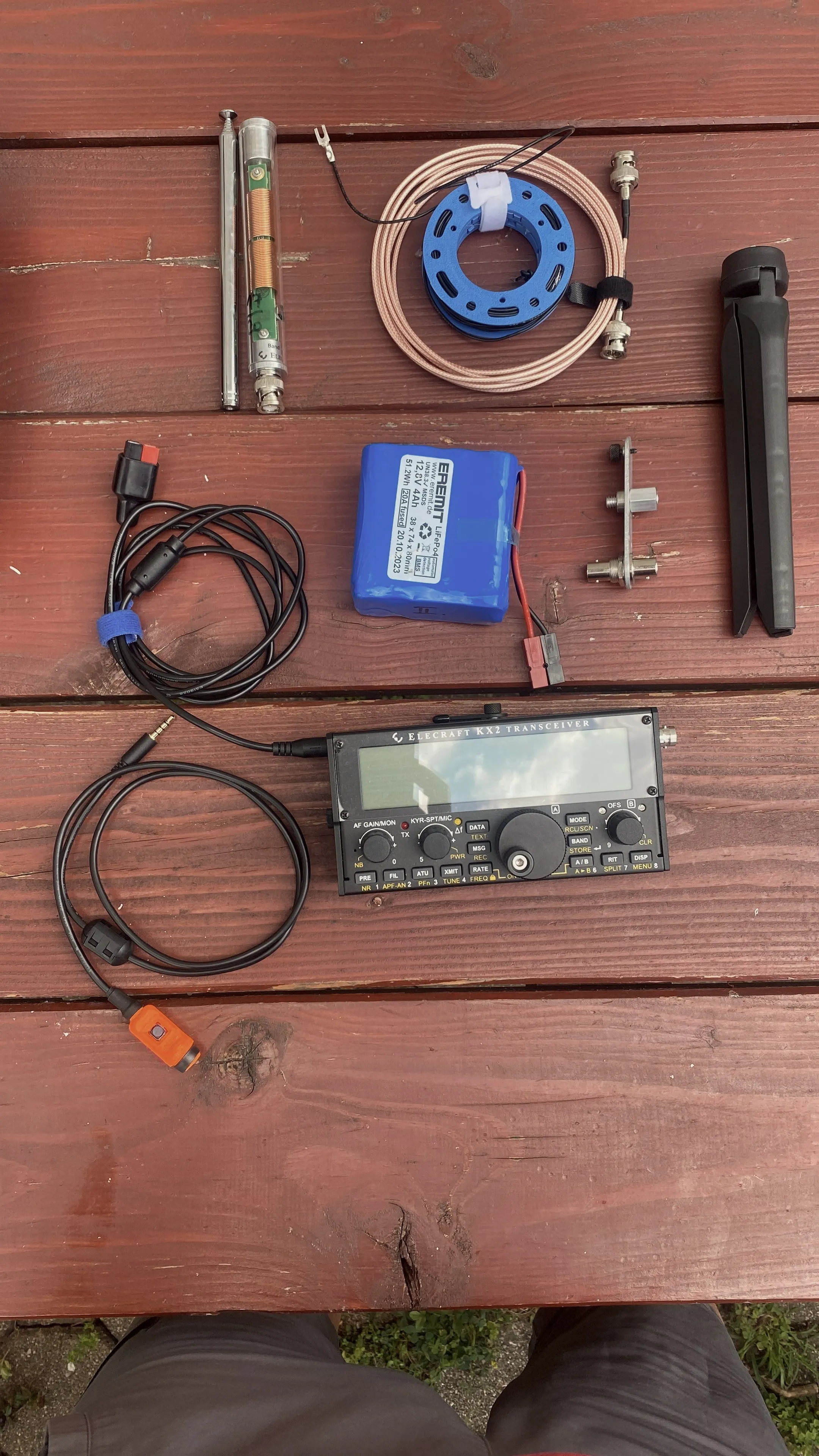 El equipo completo desplegado: KX2, batería LiFePO₄, radiador telescópico con bobina, coaxial en carrete azul, soporte de sujeción, patas plegables y cable de micrófono